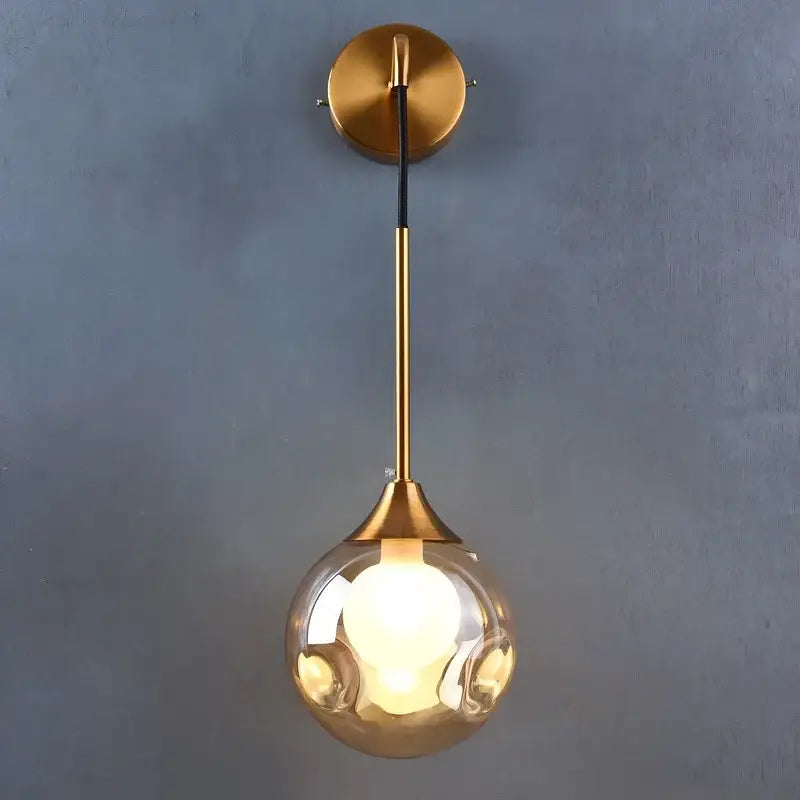 Modern gold wall sconce featuring a sleek glass ball teardrop lamp with an illuminated bulb by decorbites glass ball