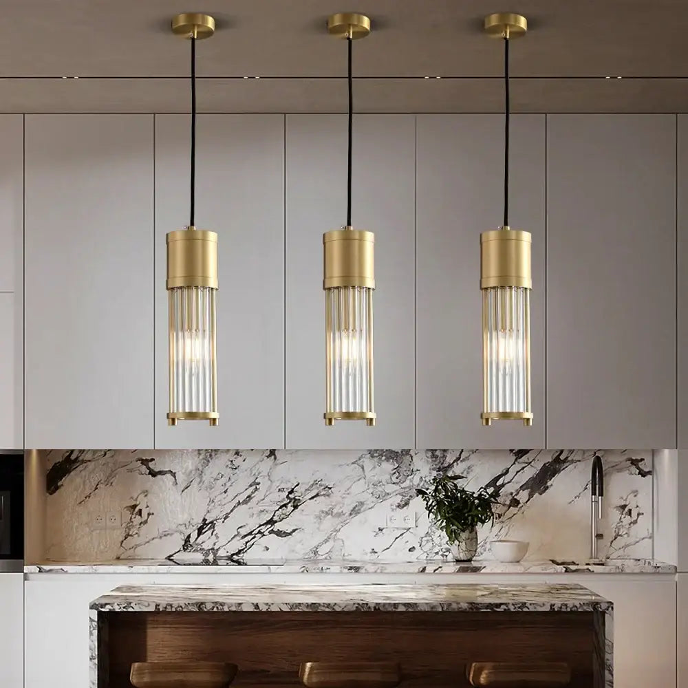 Three elegant gold-toned glass shade pendant lights with cylindrical rods hang above a kitchen island
