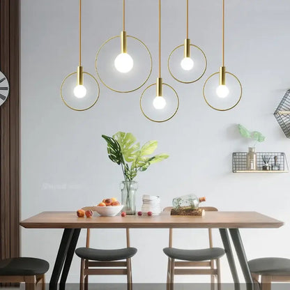 Modern gold-toned decorbites ins wind single pendant light with circular frames hanging above a wooden dining table