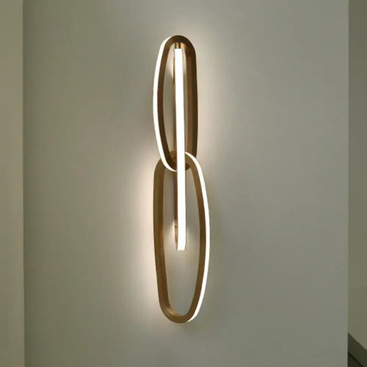 Modern gold wall lamp with two interlocking oval frames and central illuminated led strip for living room use
