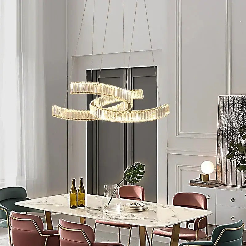 A modern gold-toned crystal led pendant light with intertwined rings hangs above a dining table by decorbites