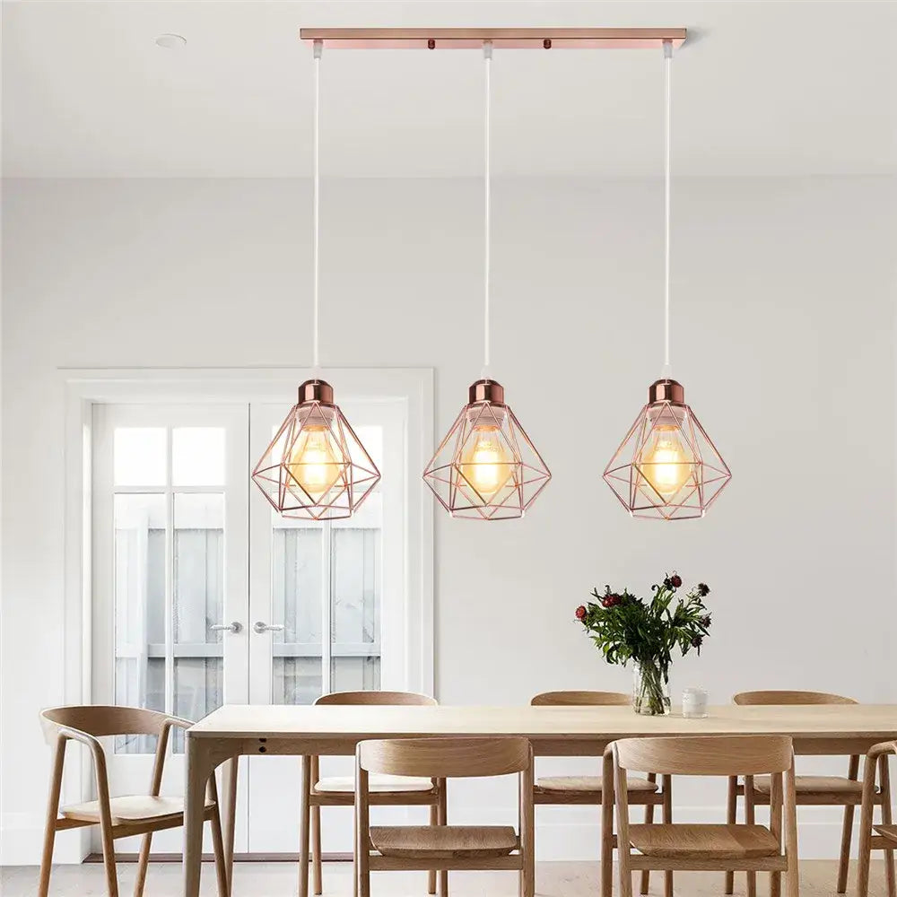 Three rose gold geometric iron frame pendant lights hang above a wooden dining table in decorbites iron frame pendant chandelier style
