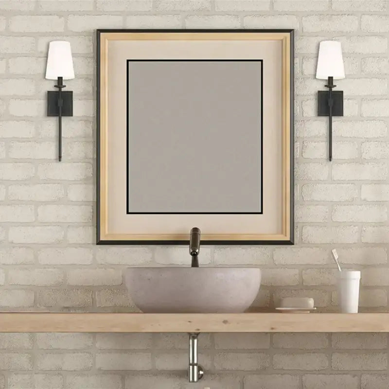A modern gold iron led wall lamp with white shade above a rectangular mirror with two-tone wood and black frame