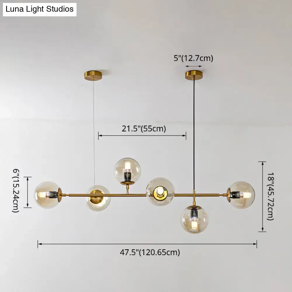 Modern gold island pendant light with gold-toned five glass globe shades and a central horizontal bar for dining room
