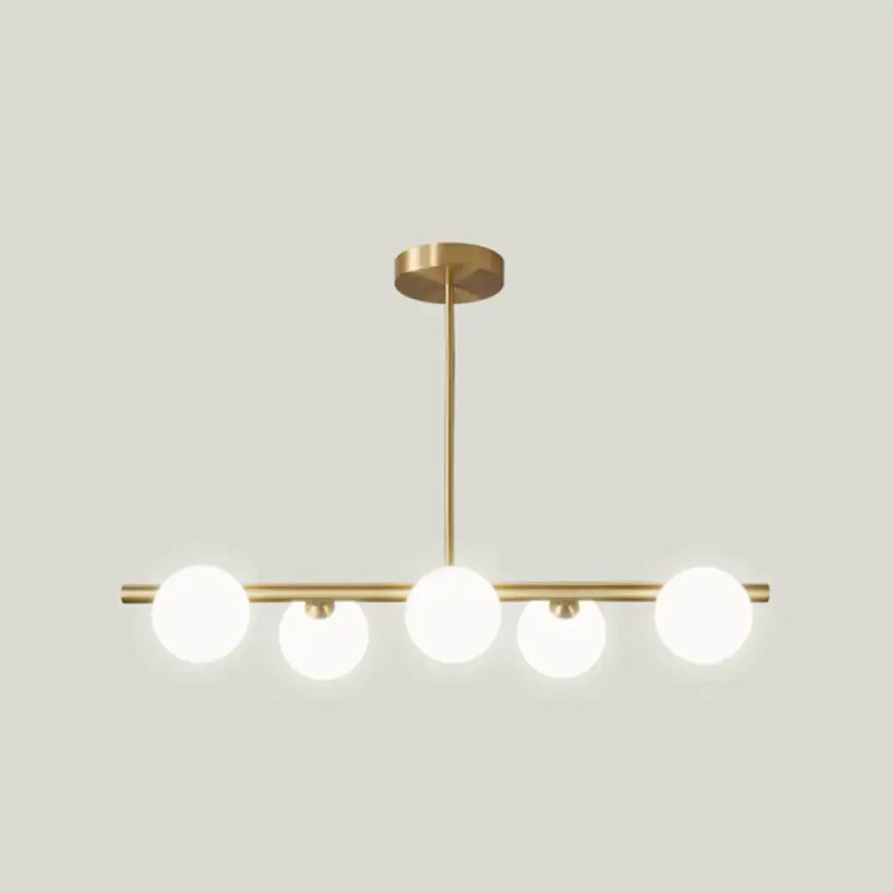 Modern gold island pendant lighting featuring brass linear design with five frosted glass globe bulbs for dining room