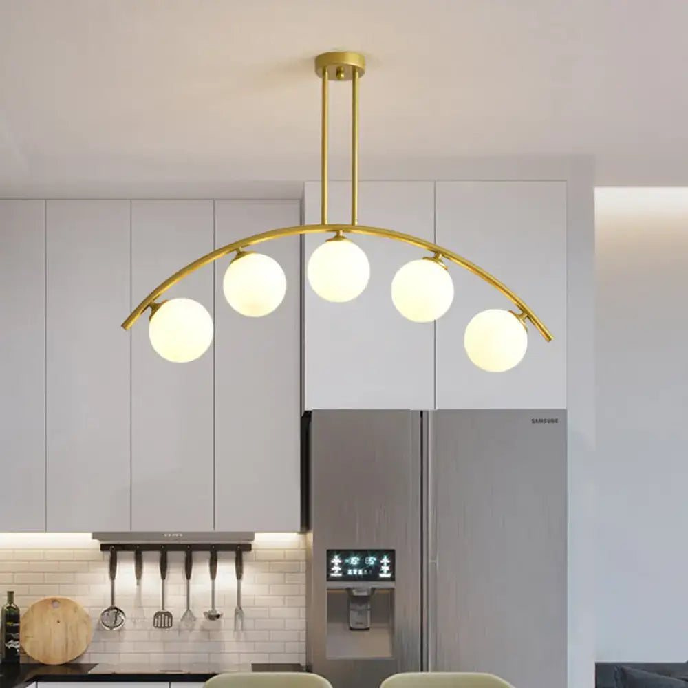 Gold-toned decorbites island pendant with five frosted glass globe bulbs and clear white shade for modern kitchens
