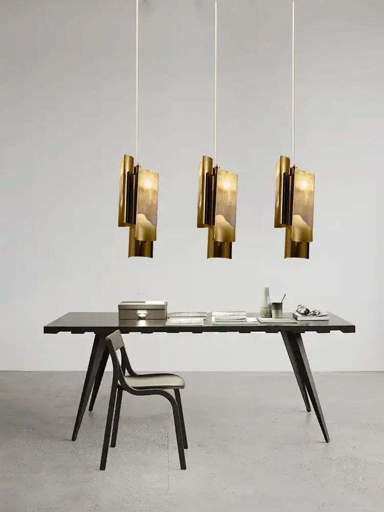 Three modern gold decorbites italian marble pendant lamps with geometric layered designs hang above a minimalist desk