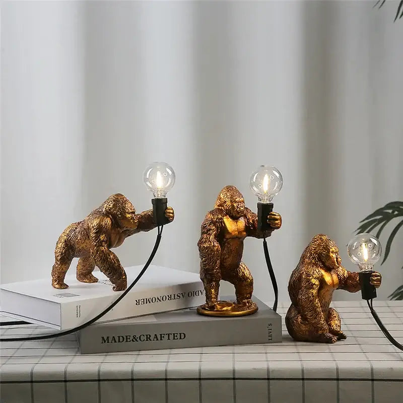 Three golden king kong resin figurines holding lit bulbs standing on books modern night light decorbites king kong