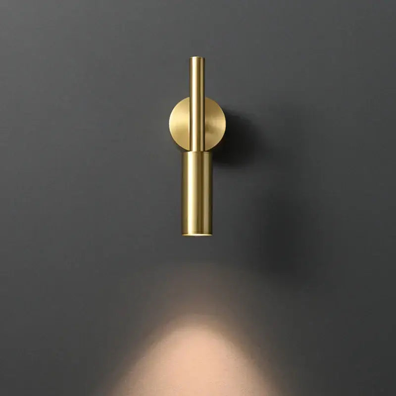 A sleek minimalist brass led wall lamp with cylindrical design and circular mount for bedroom lighting