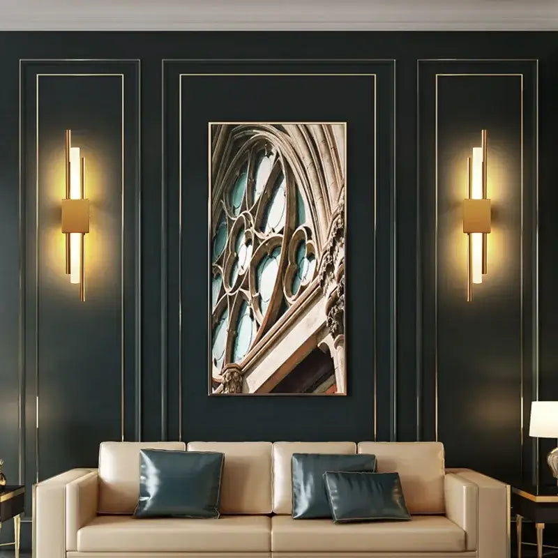 A framed gothic-style stained glass window with teal panes mounted on a dark wall near decorbites gold led wall sconce