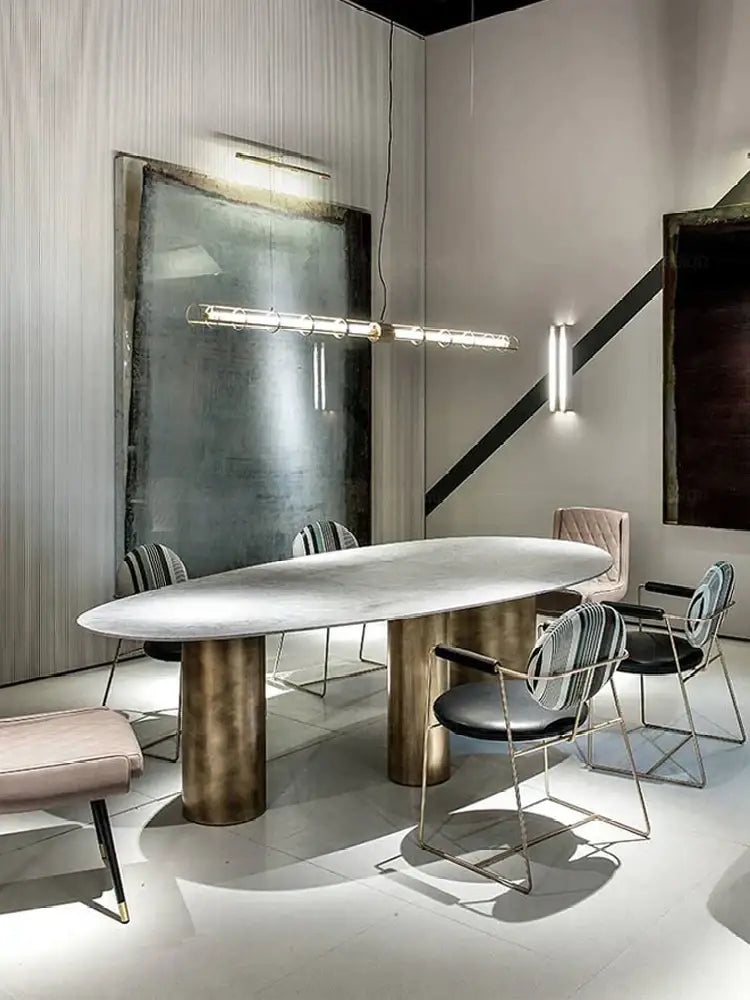 Modern gold linear decorbites glass chandelier above an oval marble dining table with bronze cylindrical legs