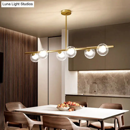 Gold-toned modern linear island light with five clear glass globe bulbs hanging from a sleek horizontal bar