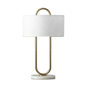 A modern gold luxury led table lamp with white cylindrical shade and u-shaped metal frame on marble base