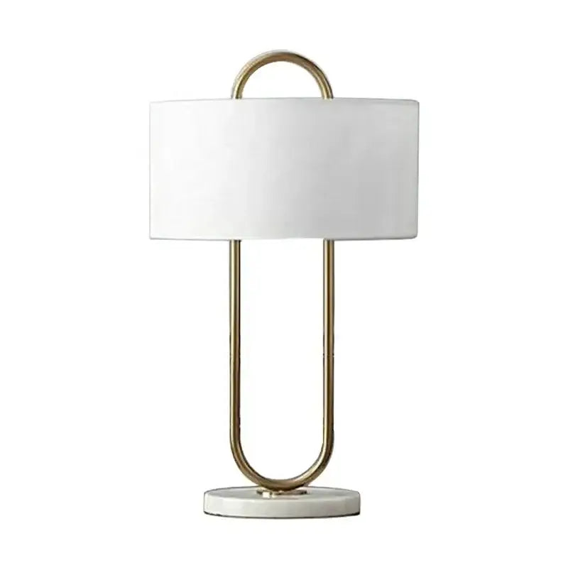 A modern gold luxury led table lamp with white cylindrical shade and u-shaped metal frame on marble base