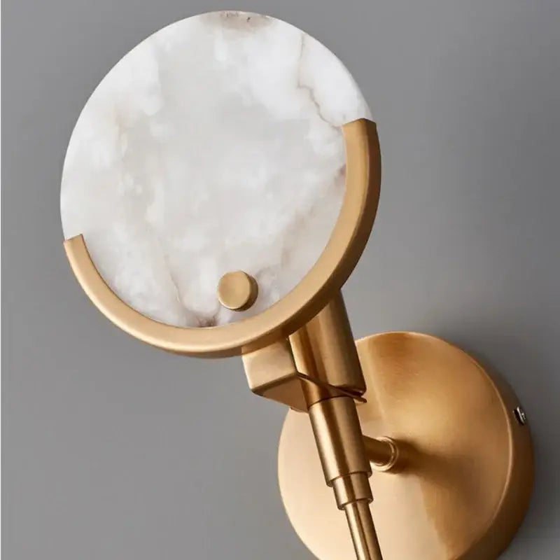 A modern wall lamp with a white marble disc and polished gold marble copper frame for minimalist bedroom decorbites