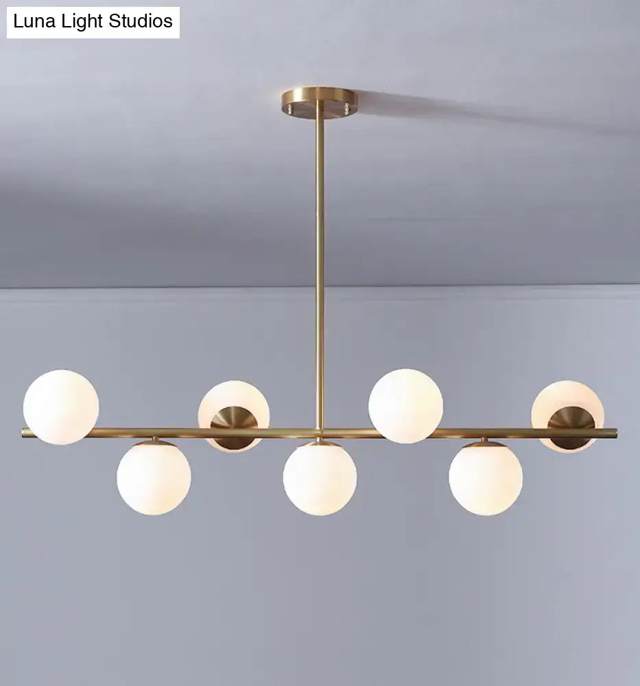 Modern gold metal chandelier with six white glass frosted globe shades in a linear pattern for dining room lighting