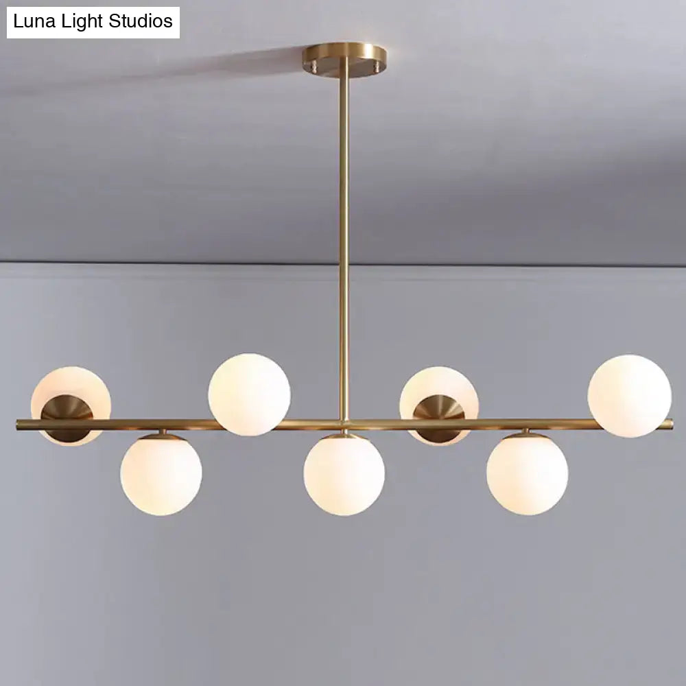 Modern gold metal pendant light with six frosted white glass globe bulbs in a linear design for dining room use