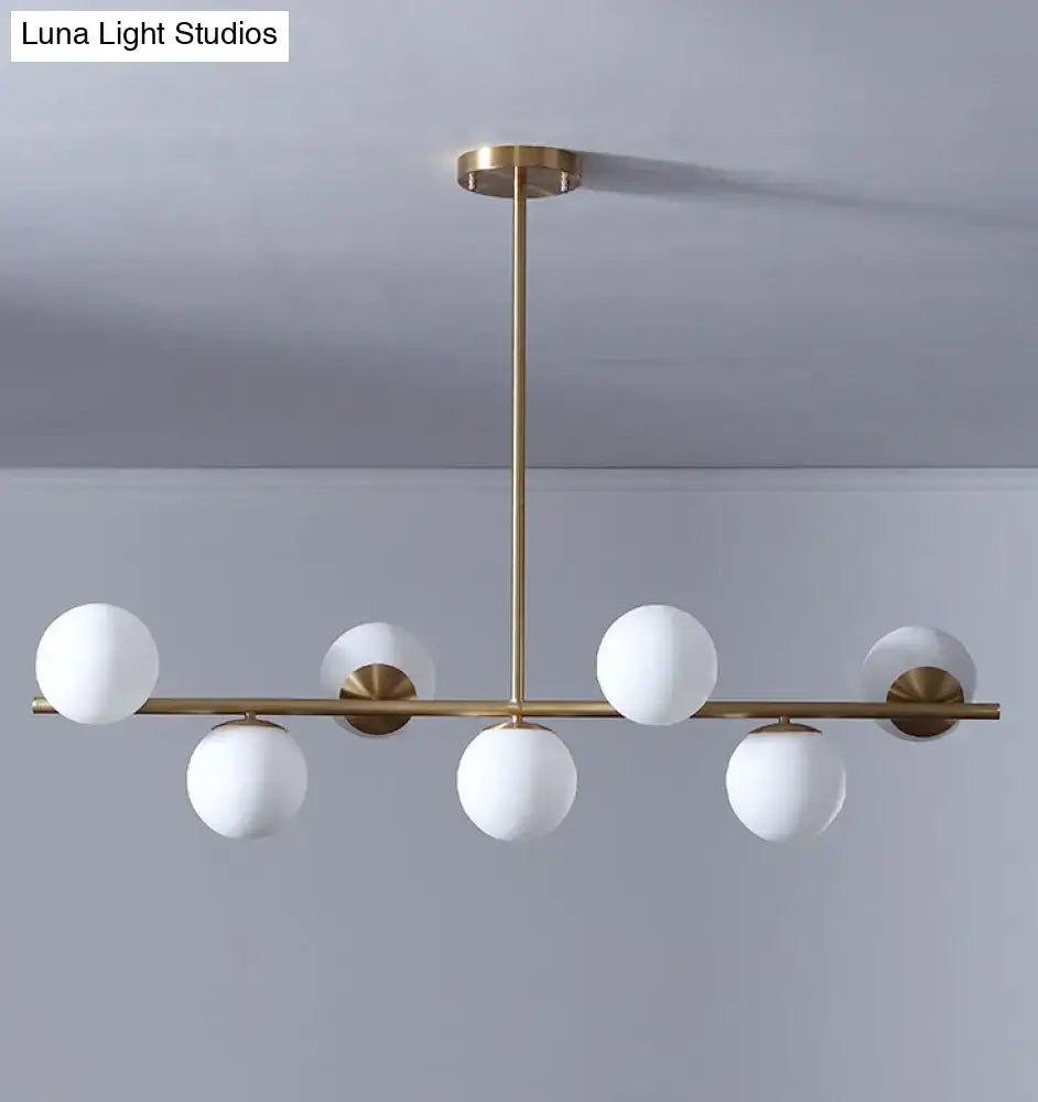 Modern gold metal pendant light with six frosted white glass globe bulbs in a linear design for dining room island