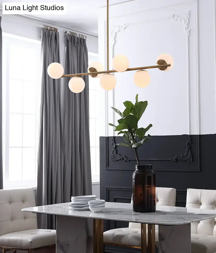 Modern gold metal pendant light with six warm-toned white glass globes for dining room island lighting