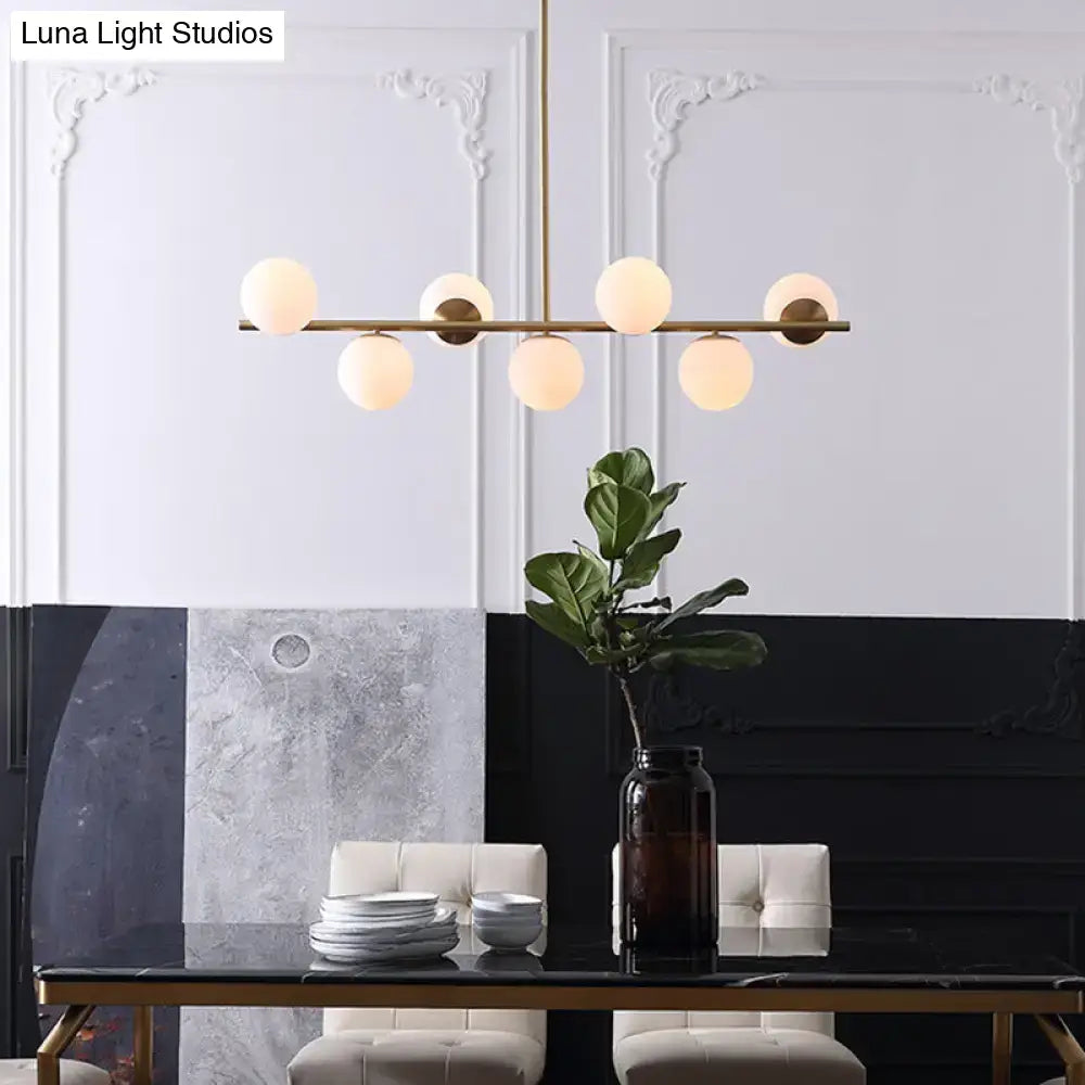 Modern gold metal six light pendant with frosted white glass globes in a linear design for dining room island lighting