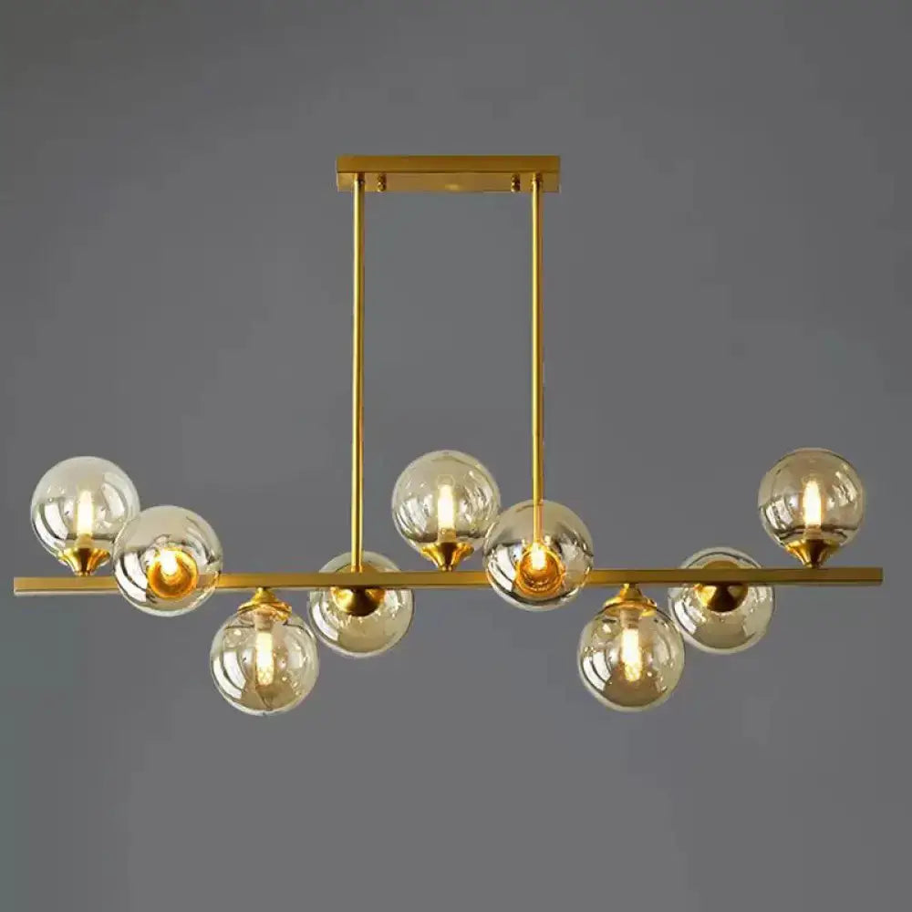 Modern gold metal chandelier with spherical amber glass bulbs suspended from a horizontal bar for dining room island lighting