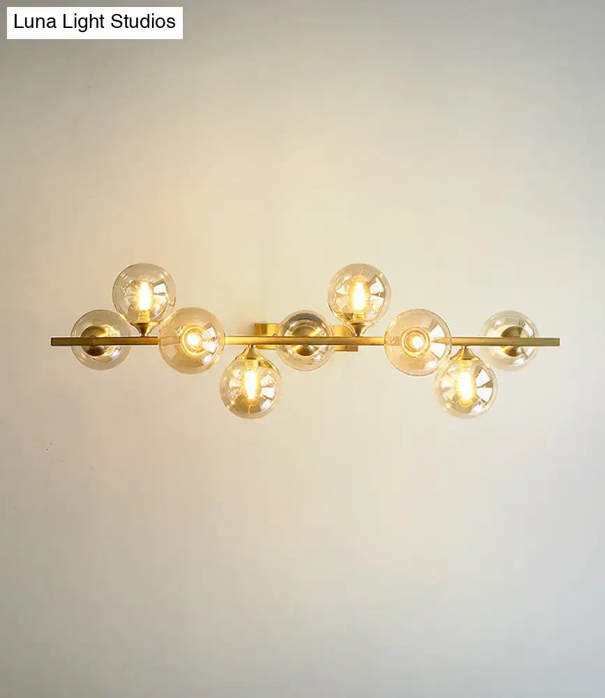 Modern gold metal wall sconce with multiple spherical amber glass bulbs on a horizontal bar for dining room lighting