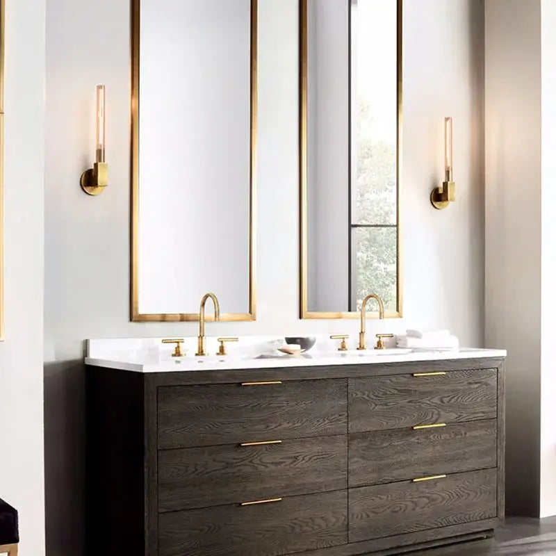 Modern gold metal and glass wall sconce light above dark wood vanity with gold hardware and white countertop in bathroom