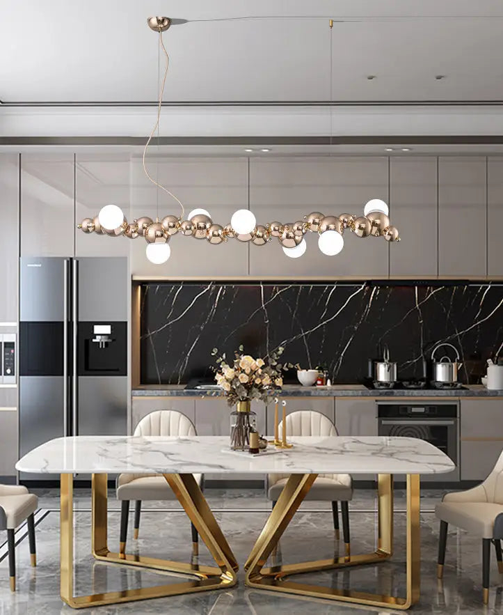 Modern gold metal ceiling light with six elongated spherical pendants hanging above dining room table