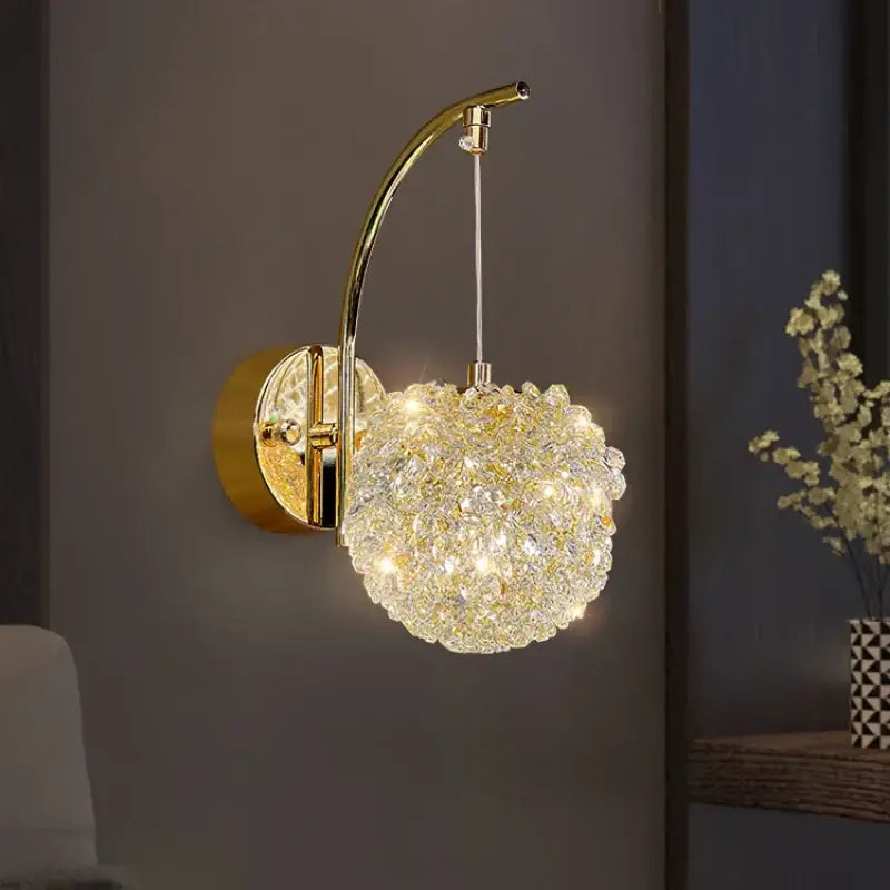 Modern gold metal crystal wall light with a curved arm and glowing spherical crystal globe for bedroom decorbites gold metal