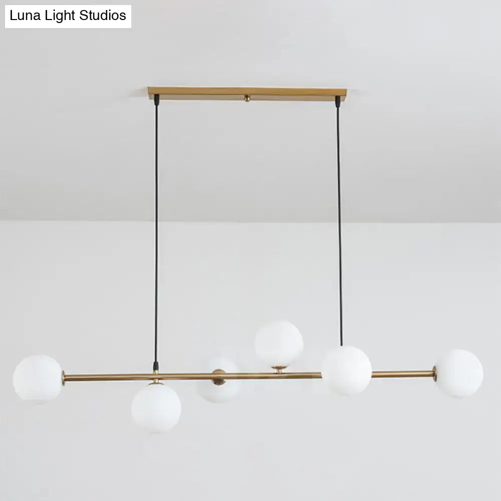 Modern gold metal island pendant with five frosted glass globes suspended by black cords from wooden ceiling mount