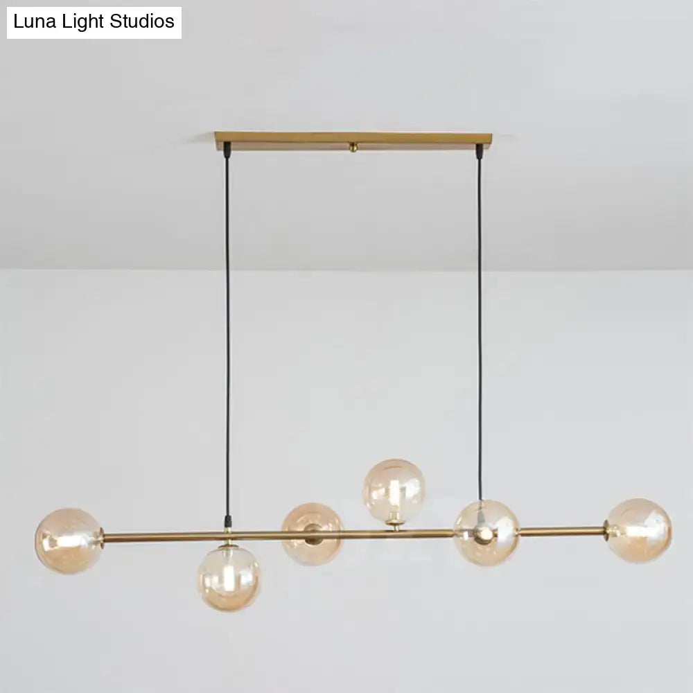 Modern gold metal island pendant with five amber glass globes and black cords for dining room lighting