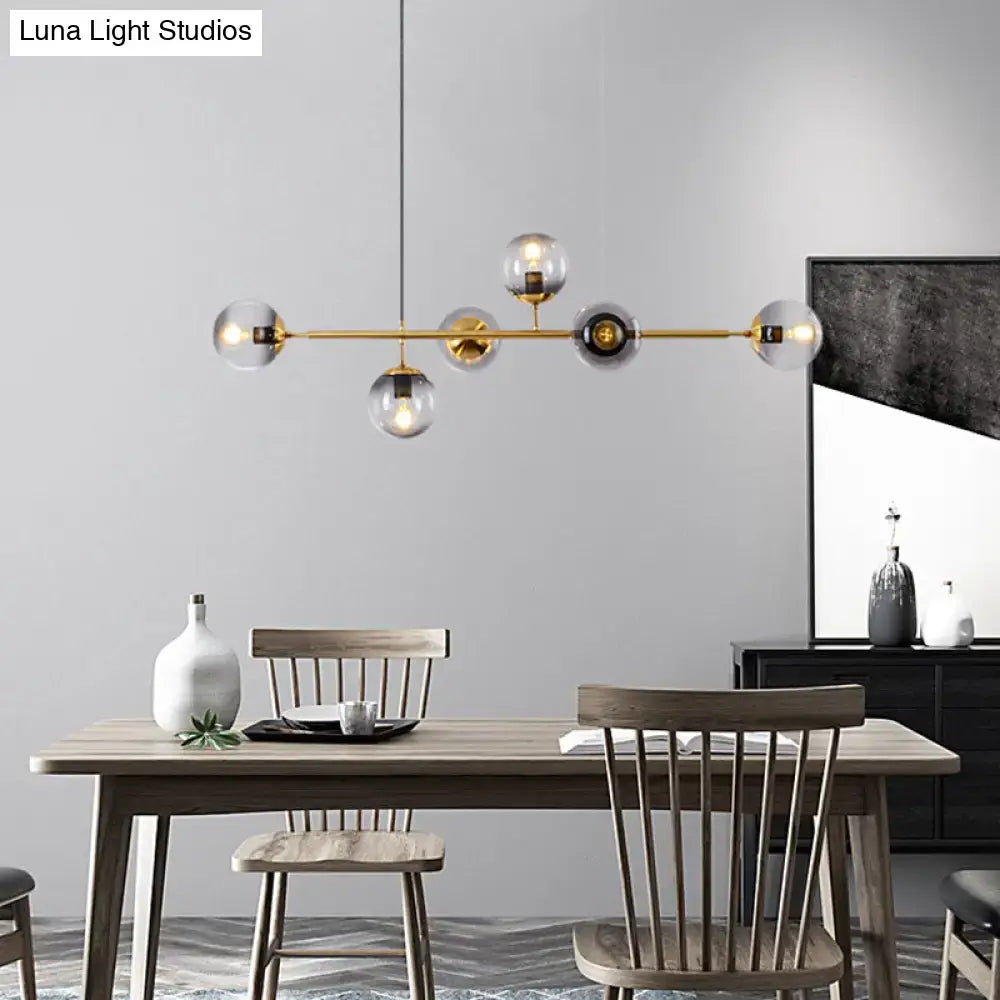 Modern gold metal island pendant with blue glass spheres and brass globes hanging above wooden dining table
