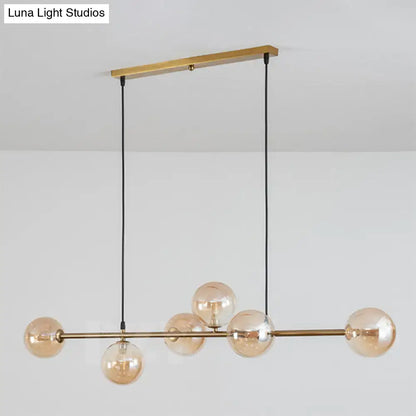 Modern gold metal island pendant with six amber glass globes suspended by black cords for dining room lighting