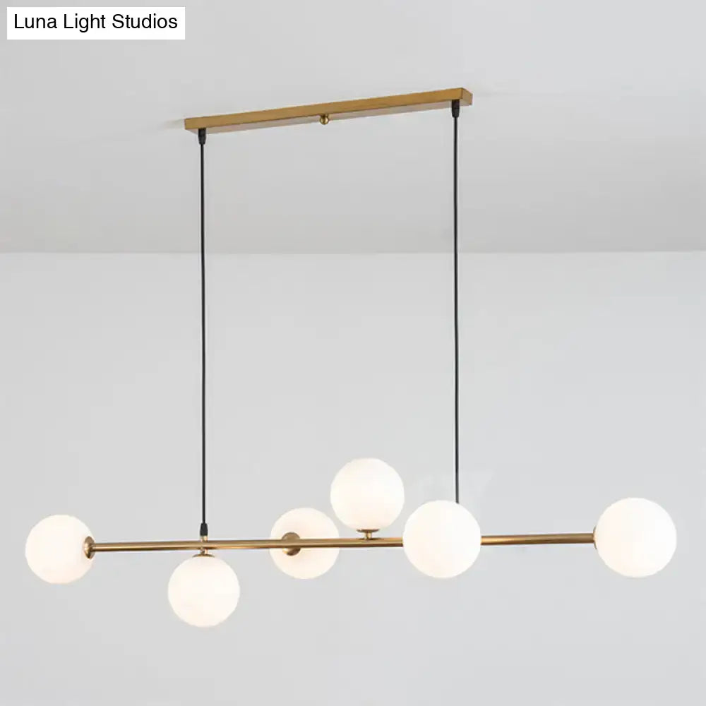Modern gold metal island pendant with five frosted glass globes suspended by black cords for dining room lighting