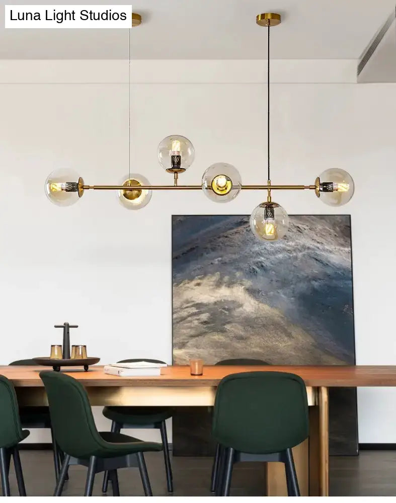 Modern gold metal island pendant with brass finish and clear glass globe shades featuring exposed filament bulbs for dining room