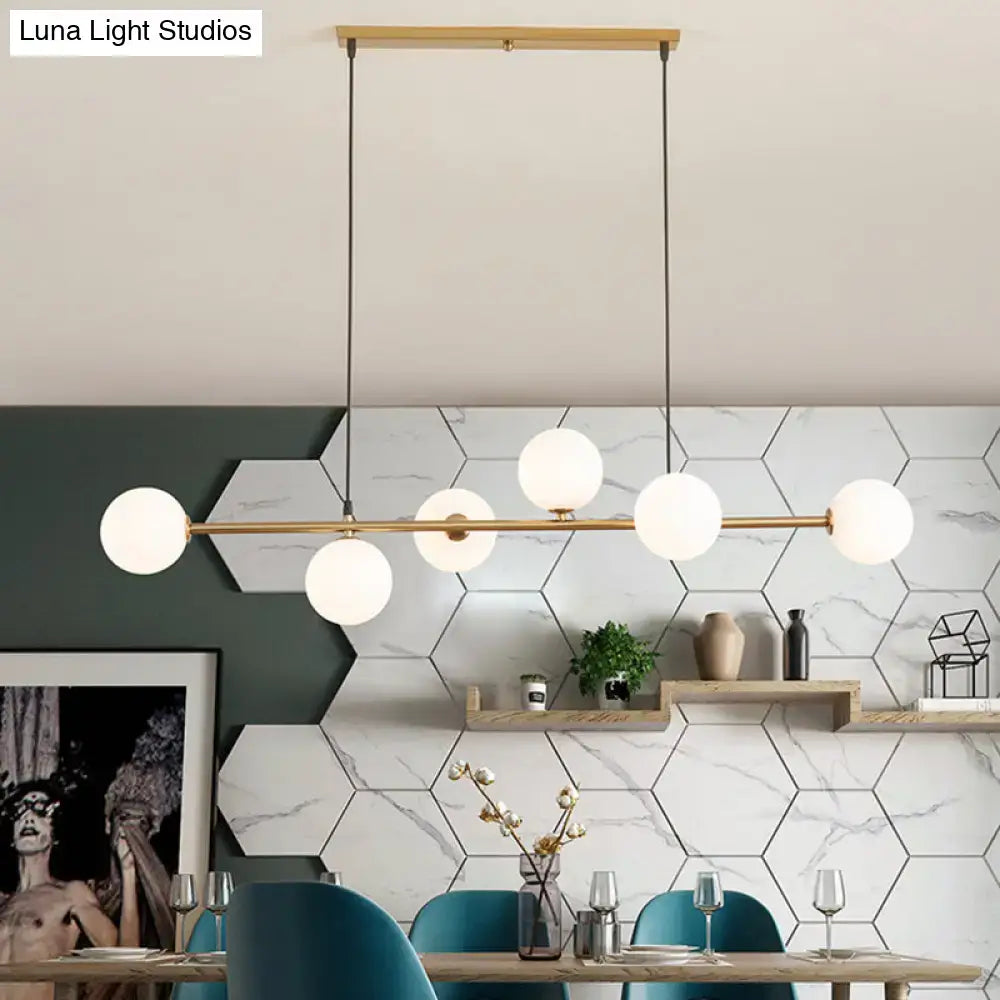 Modern gold metal island pendant featuring six frosted glass globe bulbs on a horizontal bar for dining room use