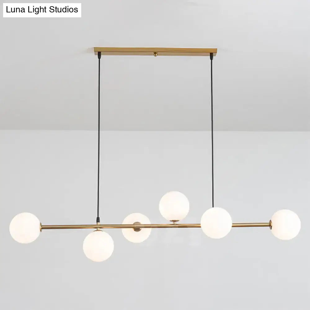 Modern gold metal island pendant with five frosted glass globe bulbs suspended by black cords for dining room