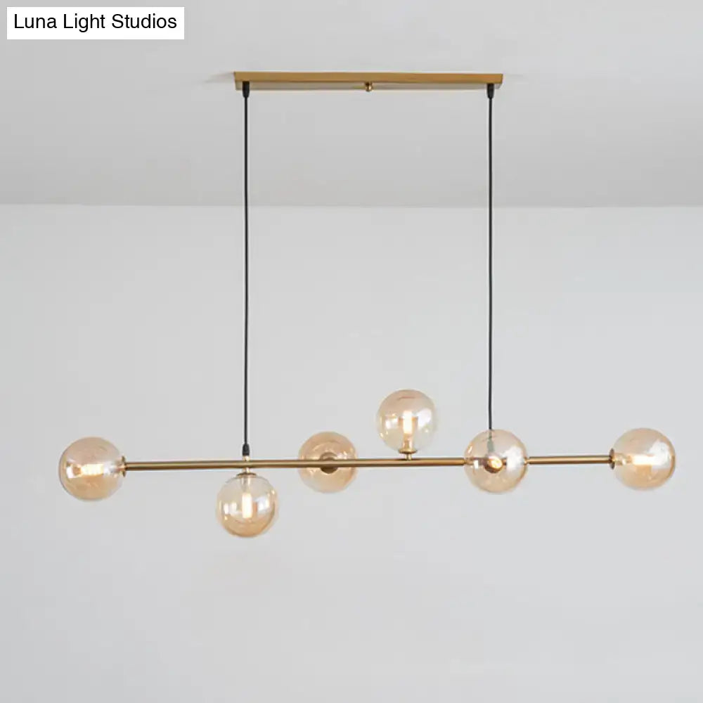 Modern gold metal island pendant light with five amber glass spheres suspended by black cords for dining room use