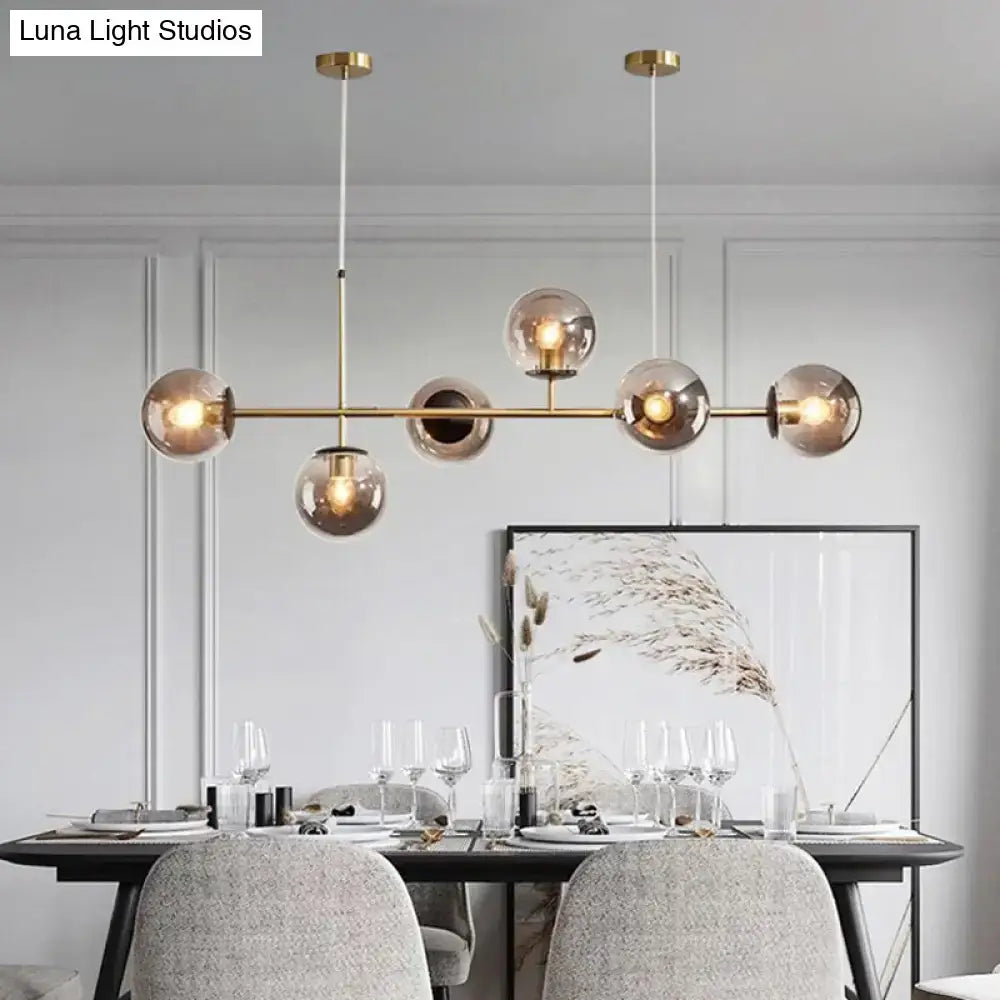 Modern gold metal island pendant with brass-toned frame and six smoked glass globes suspended by thin cords for dining room