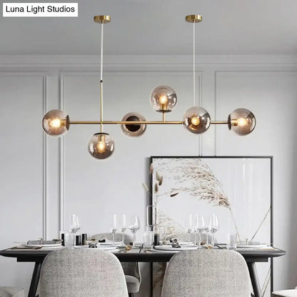 Modern gold metal island pendant with brass-toned frame and six smoked glass globes suspended by thin cords for dining room