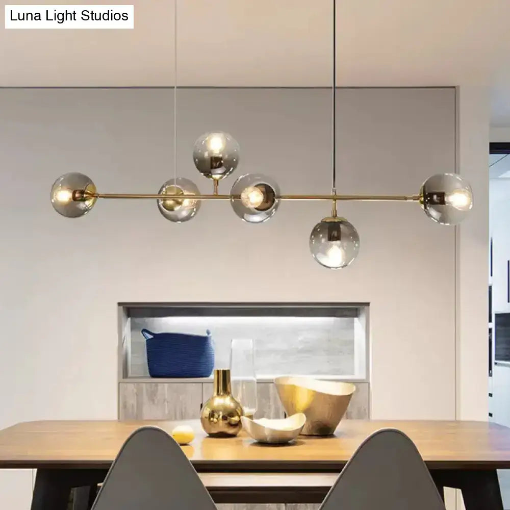 Modern gold metal island pendant with five clear glass globes suspended from a central rod for dining room use