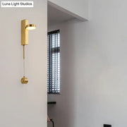 Modern gold metal wall sconce with a sleek rectangular base and adjustable circular head emitting warm white light