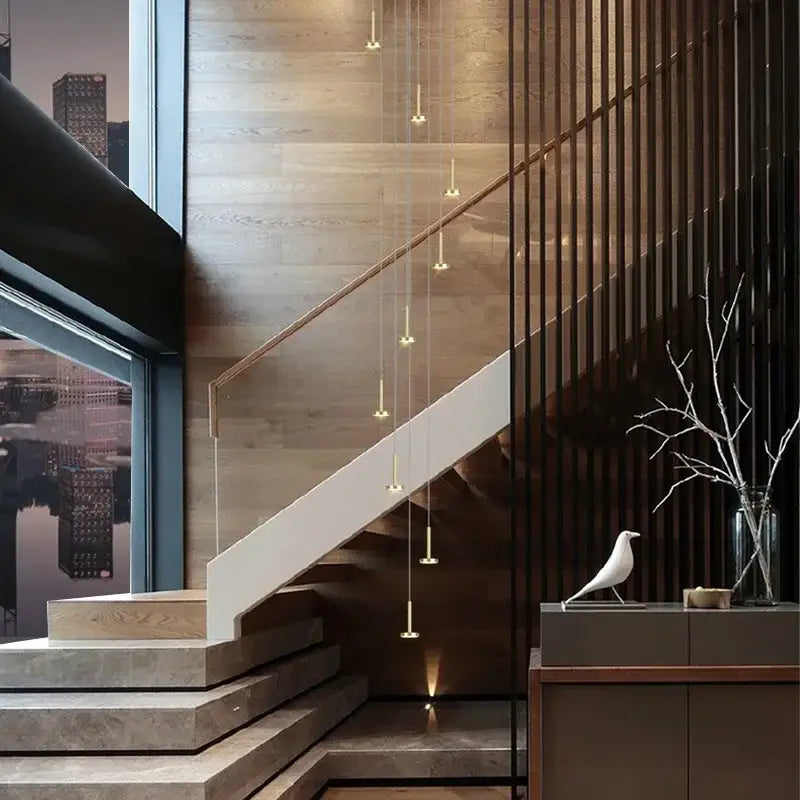 A sleek modern staircase with white handrail and wooden steps illuminated by a gold minimalist ceiling chandelier