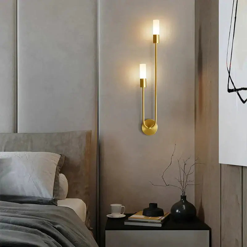 Modern gold-toned led wall lamp with two vertical cylindrical lights and a curved minimalist design for bedroom use