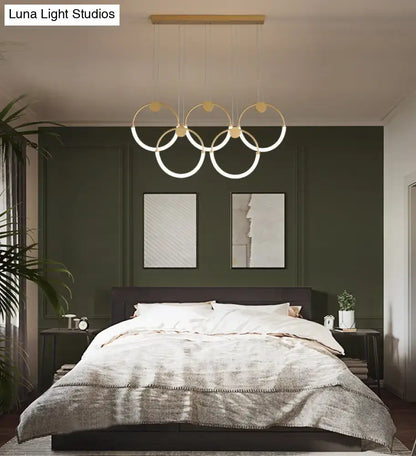 Modern gold minimalistic ring pendant light with illuminated circular rings suspended above a bed for living room