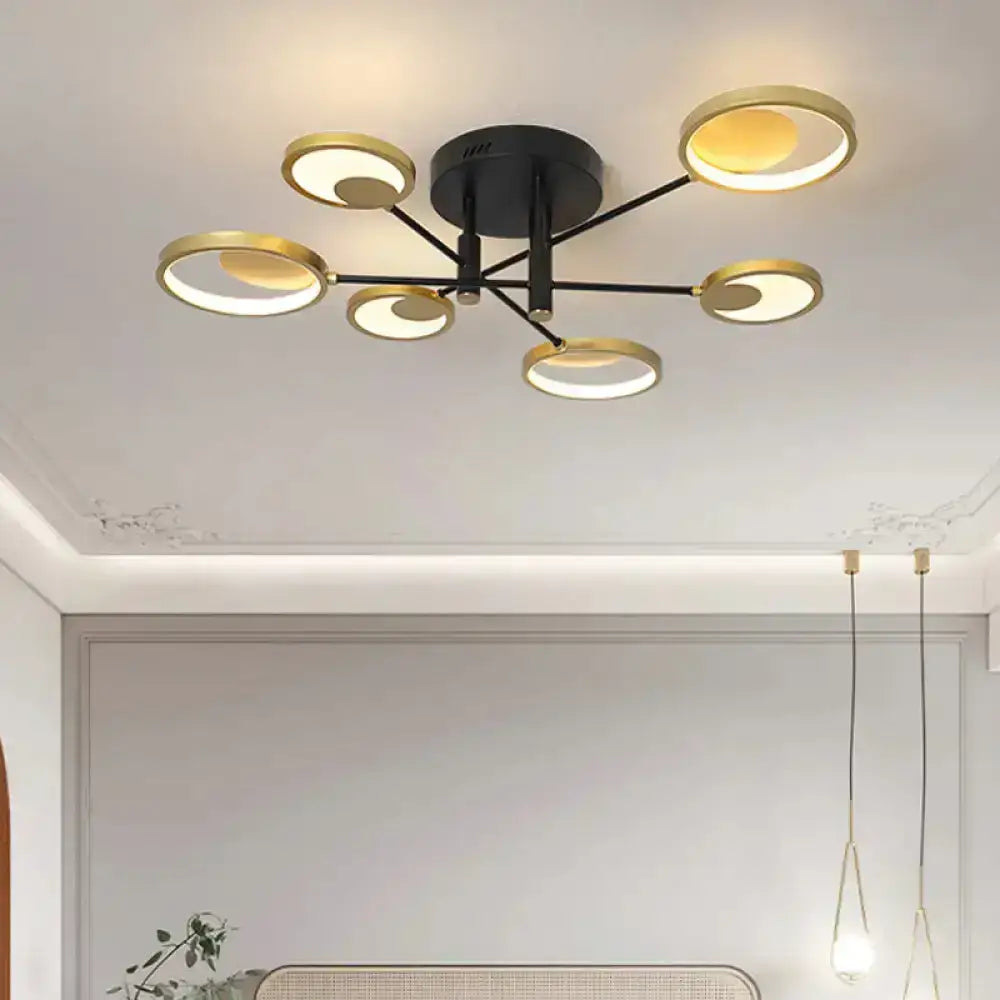 Modern gold molecule ceiling mount chandelier with six circular gold-toned rings and black arms emitting warm glow