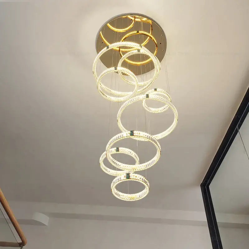 Modern gold multi tier duplex crystal chandelier with glowing rings suspended from a circular ceiling mount for living room