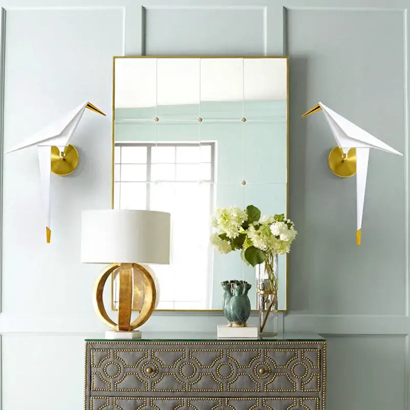 Gold-framed rectangular mirror with grid panels and brass rivets paired with modern gold origami bird led wall lamp