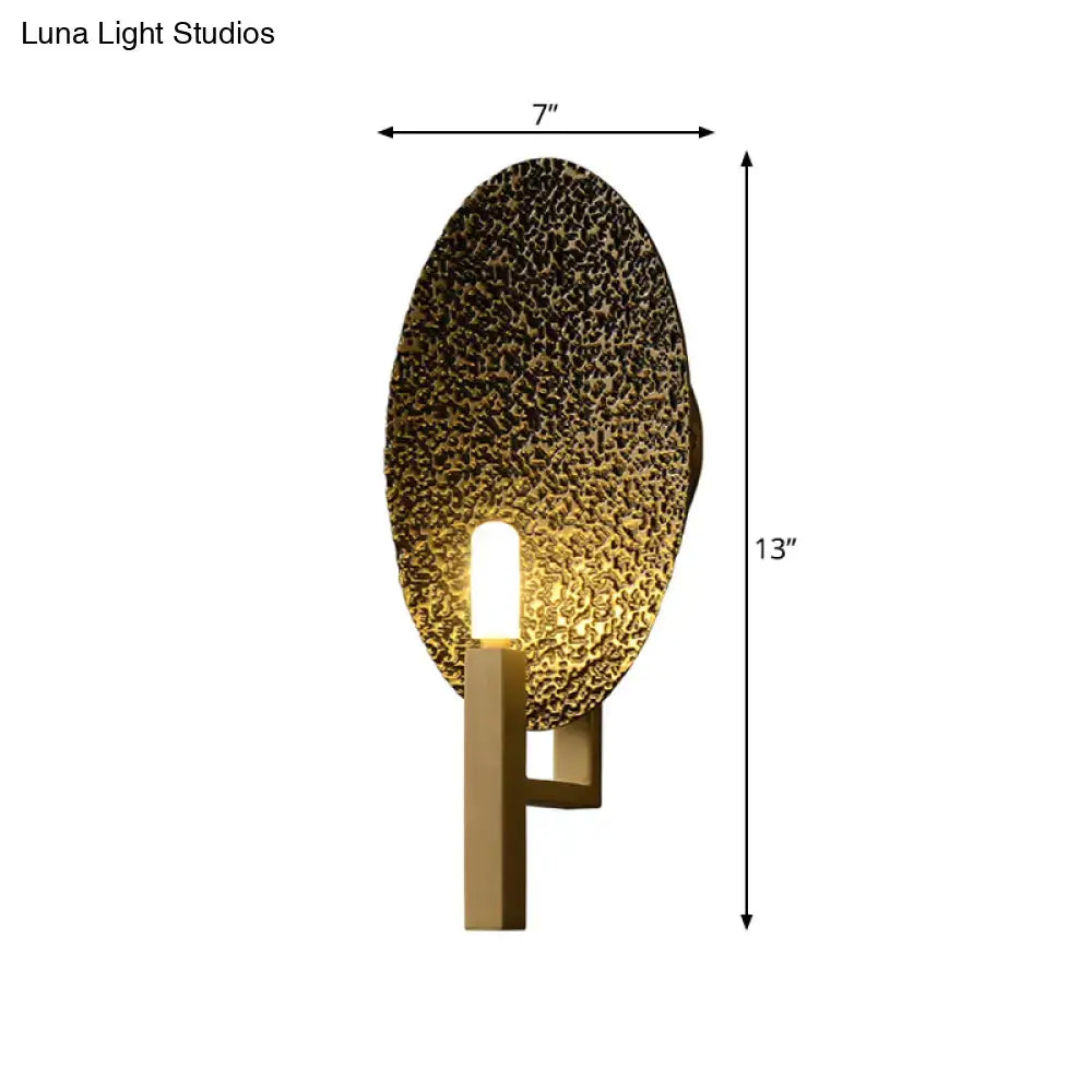 Modern gold oval metal wall sconce with textured hammered finish and sleek rectangular base for bedroom lighting