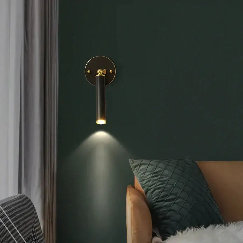 Black cylindrical wall sconce with gold-toned base and brass accents emitting warm light in modern wall sconce set
